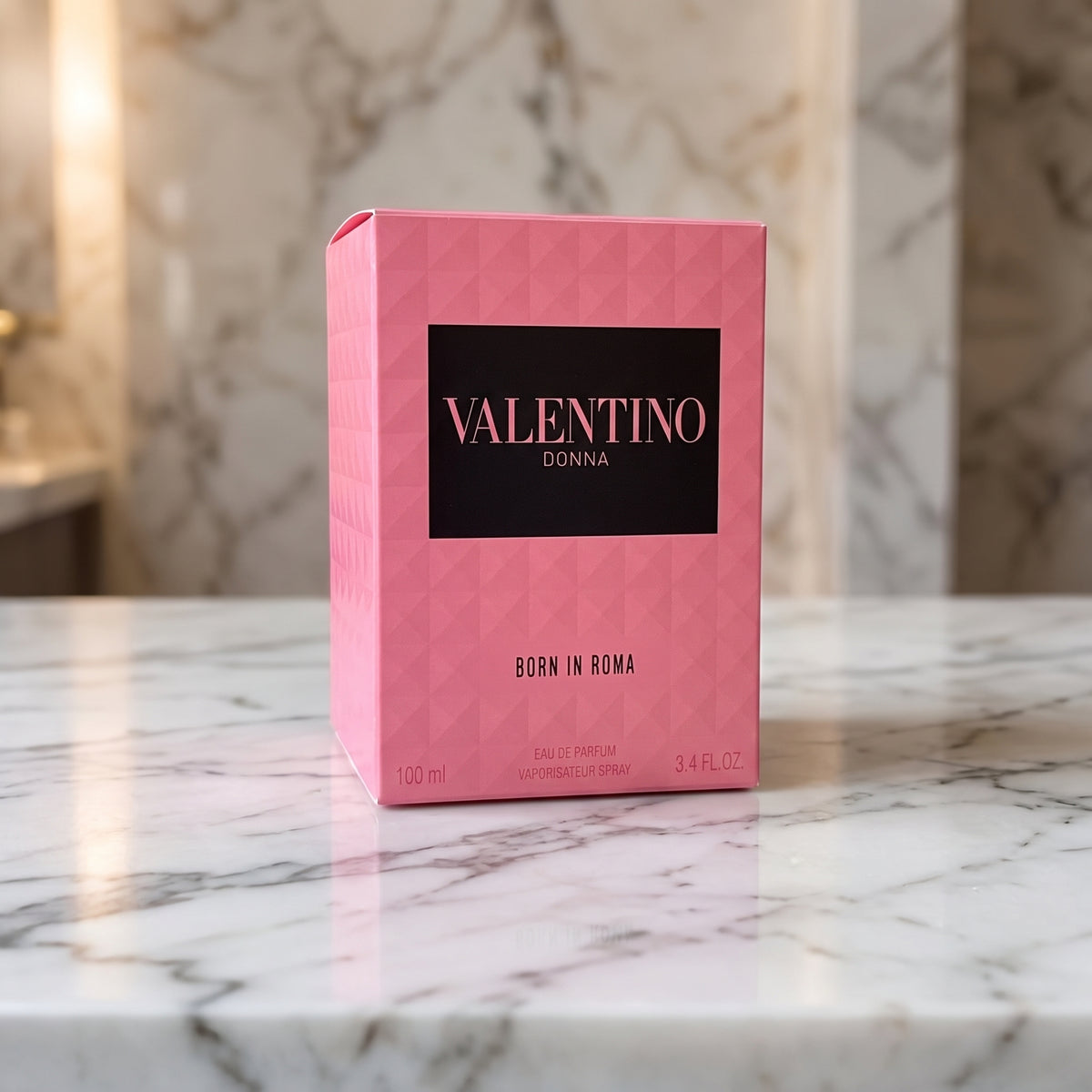 A pink Valentino Donna perfume box with a black front label, standing on a white marble countertop with a blurred marble wall background.