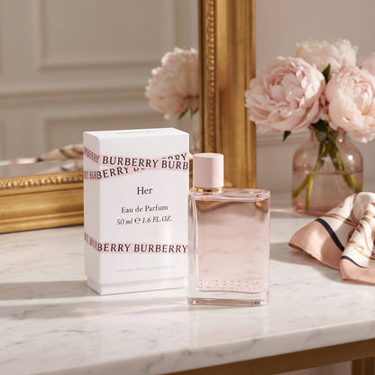 Burberry Her Eau de Parfum 50ml bottle with its white packaging box, styled on a marble surface next to a gold mirror, pink peony flowers, and a pink striped scarf.