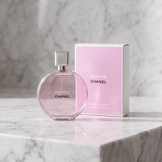 Chanel Chance Eau de Toilette perfume bottle in a round glass shape with a silver cap, standing next to its pink packaging box on a white marble surface.