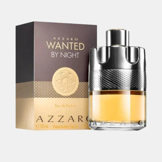 Azzaro Wanted By Night Eau de Parfum bottle with its retail box, displayed on a light gray background. The bottle features a textured silver cap and neck, filled with amber-colored liquid, while the box is dark brown and gold.