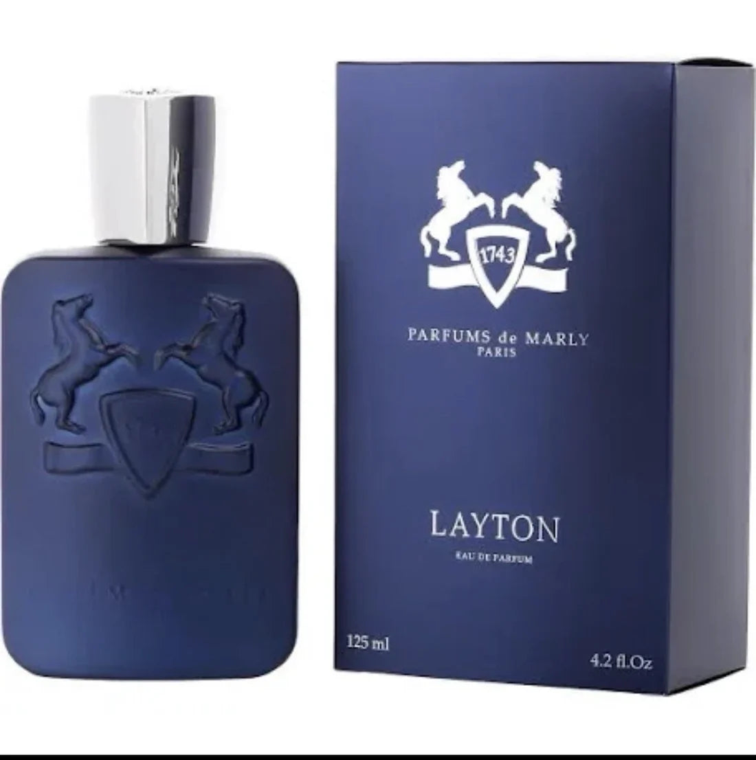A bottle of Parfums de Marly Layton Eau de Parfum in a dark blue bottle with a silver cap, shown next to its matching dark blue box featuring a white horse emblem.